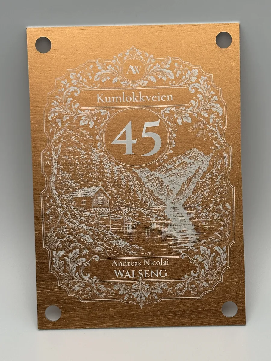 Husskilt i kobberfarget aluminium, 105 × 150 mm med fire hull: ornamentramme, husnummer 45, gatenavn, navn og et gravert fjordmotiv