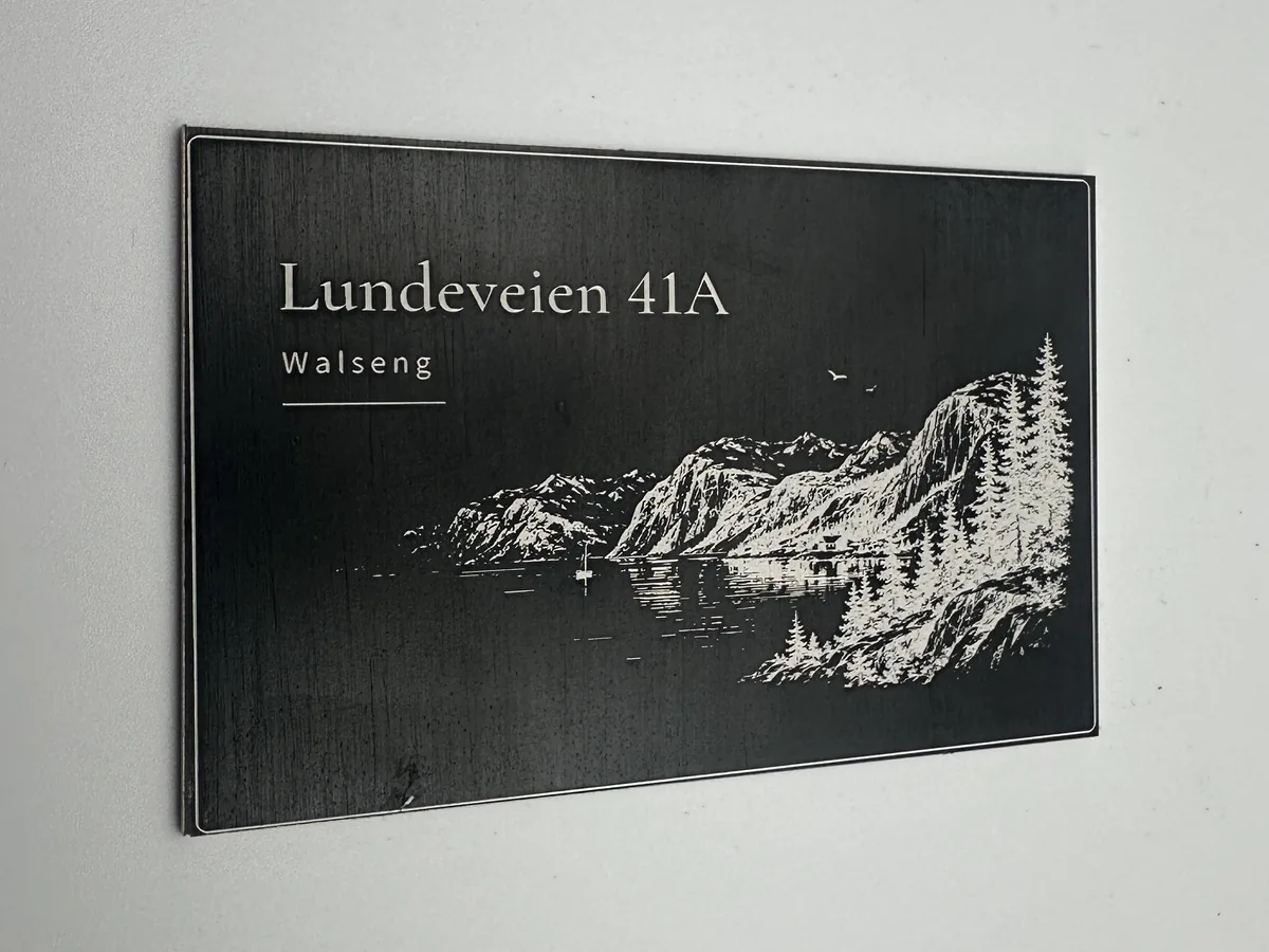 Sort aluminiumsskilt med designforslaget «Fjord»: adressen Lundeveien 41A, navnet Walseng og et gravert fjordlandskap