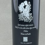 Gravert vinflaske som bryllupsgave eller takkegave med motiv av et brudepar og blomster. Teksten lyder: «Gode minner skapes sammen», med hilsen fra Thomas og Emilie.