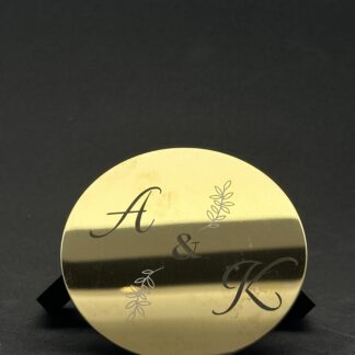 Bordbrikke eller drikkebrikke i messing med gravert motiv. motivet som er gravert er navnet hytte og koordinater med en kompassnål.